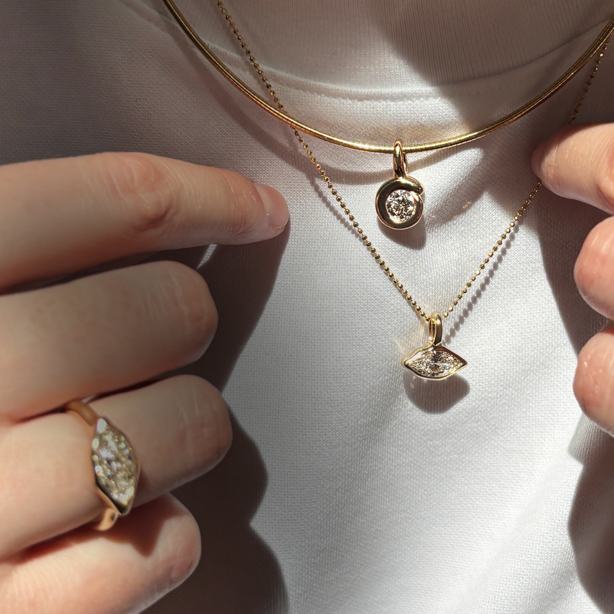 A model wears 14K recycled yellow gold charms and chains from AMANDA PEARL. A quill bezel charm with lab grown diamond on an omega chocker. A marquise diamond charm won a diamond cut bead chain, and a marquise diamond ring.