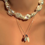 A model wears a Baroque Pearl collar, styled with a diamond cut bead chain in white gold, the pear molten solitaire charm in white gold, and the mother of pearl drop charm in white gold.