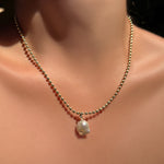 Chunky bead chain necklace and mini baroque pearl charm on a model's neck.