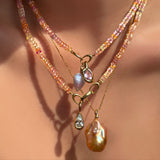 Blush sapphire necklaces layered with matching gemstone, diamond, and baroque pearl charms on a model's neck.