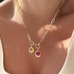 Gold chunky paperclip chain necklace with two gemstone pendants on a person wearing a beige top.
