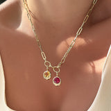 Gold chunky paperclip chain necklace with two gemstone pendants on a person wearing a beige top.