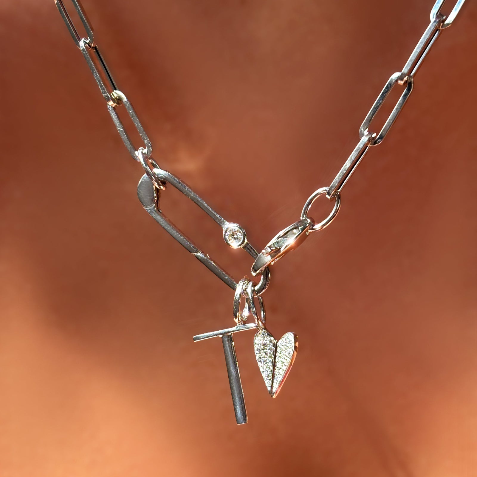 Chunky paperclip chain necklace with letter charm, mini full pave folded heart charm, hanging from a paperclip charm lock with diamond in white gold on the neck.