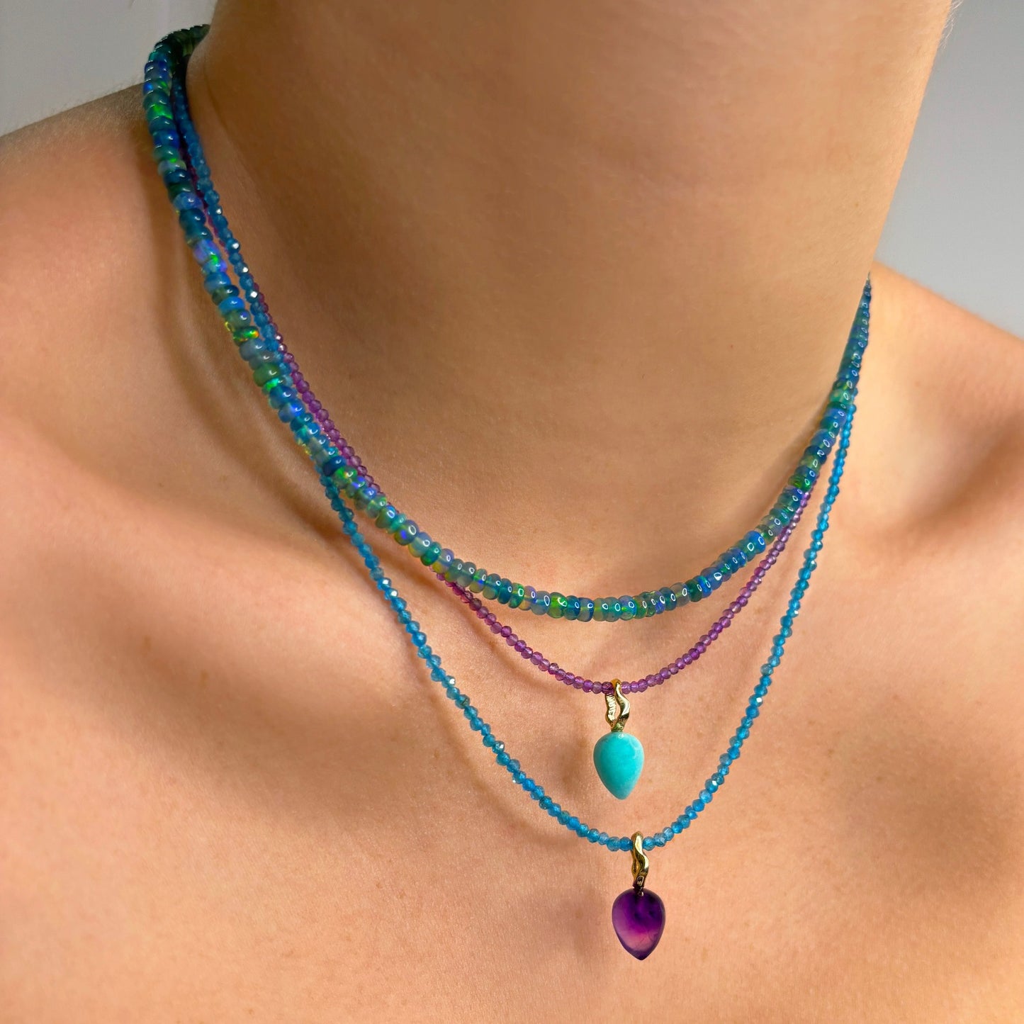 Two shimmering beaded necklaces made of 2mm faceted opals in shades of purple and bright blight blue. Styled on a neck layered with two acorn drop charms.