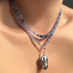 denim blue faceted sapphire necklaces with white gold linking ovals clasp dropping a silvery lunar baroque pearl charm on ripple bale on a model's neck.