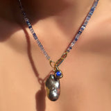 Denim faceted sapphire opal necklace with sapphire charm lock holding a lunar baroque pearl and molten knot charm with star sapphire on a model's neck.