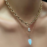 A model wears a drop link chain in 14k yellow gold from which hangs a diamond pear charm with a yellow gold bezel. A diamond cut bead chain hangs around the models neck as well and off of it hangs a gold ripple bale moonstone gemstone drop charm. 