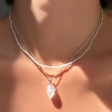An AMANDA PEARL White Zircon slim gemstone necklace layered over a white gold diamond cut bead chain with rainbow moonstone drop charm on a model's neck.