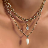A model wears a drop link chain necklace in yellow gold, a 6mm irregular cable chain, and a bead chain from which hangs a quill bezel solitaire charm with a diamond also in yellow gold.  