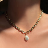 Chunky gold drop link chain necklace with a mini baroque pearl charm hanging from it, worn on a model's neck.