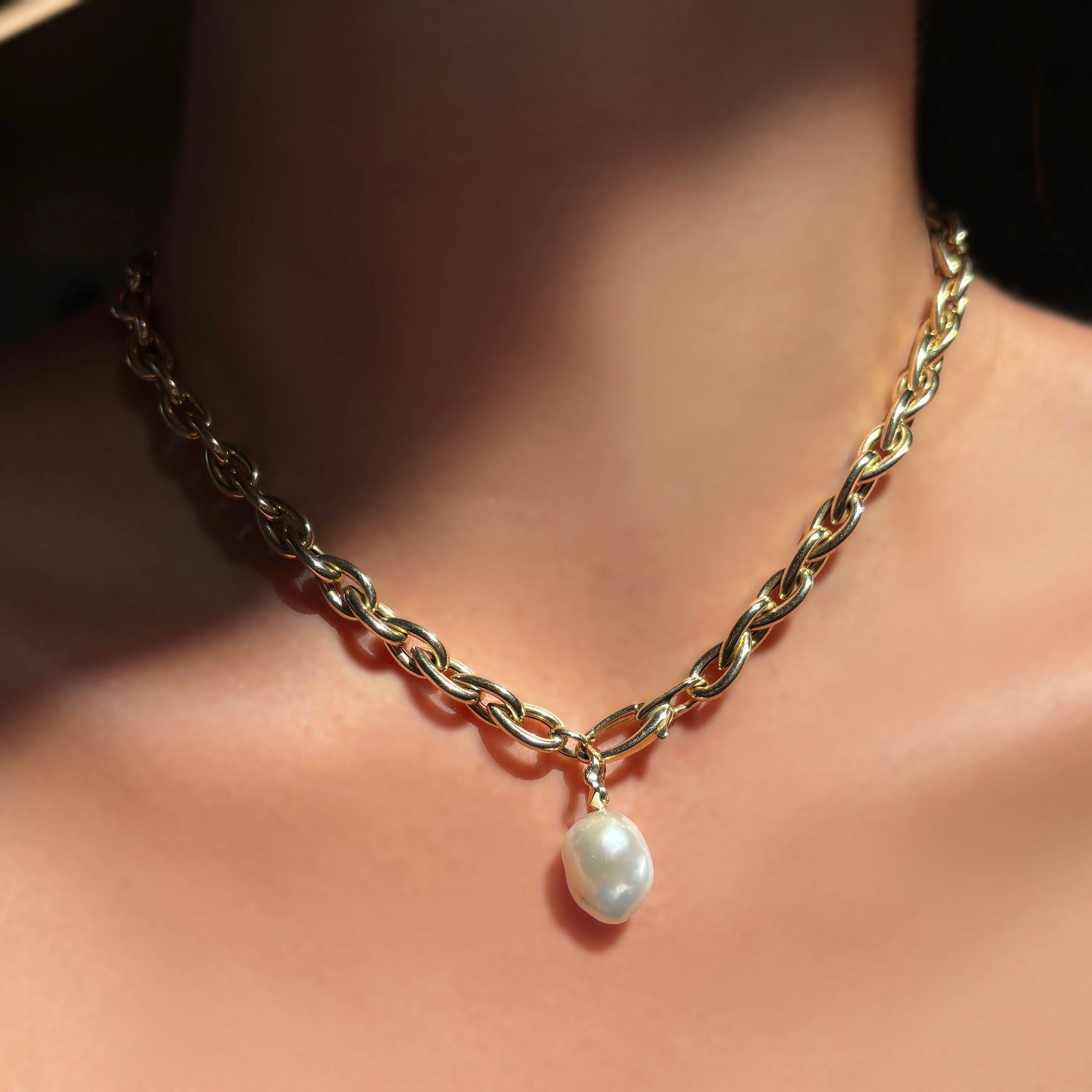 Chunky gold drop link chain necklace with a mini baroque pearl charm hanging from it, worn on a model's neck.