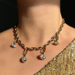 Drop link chain necklace with molten solitaire charms with marquise, round, oval diamonds hanging from small diamond charm locks on a model's neck, paired with a gold sequin top.