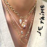 A close up of a model wearing a layered look of two 14K yellow gold chains, a pale pink opal necklace. From these necklaces hang 14k recycled gold letter charms reading "X" and "O" a molten pear diamond charm with a yellow gold bezel, an irregular baroque pearl charm in blush, a mother of pearl charm and a pale pink opal charm with gold ripple bails.