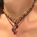 Gold chain necklace with a red gemstone pendant on a model.