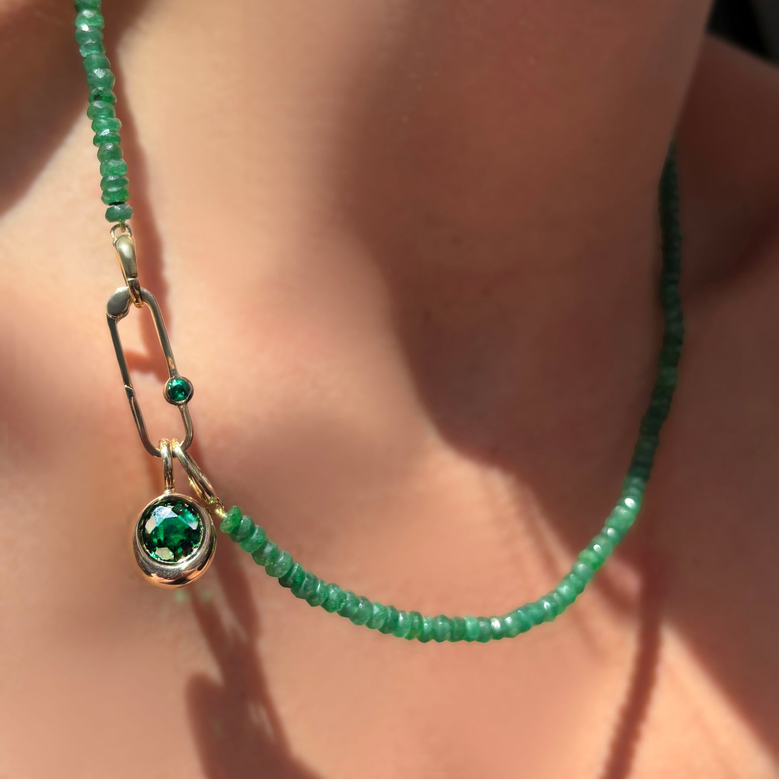 Faceted Emerald necklace with paperclip charm lock with emerald hanging a molten solitaire charm with round emerald on a model's neck.