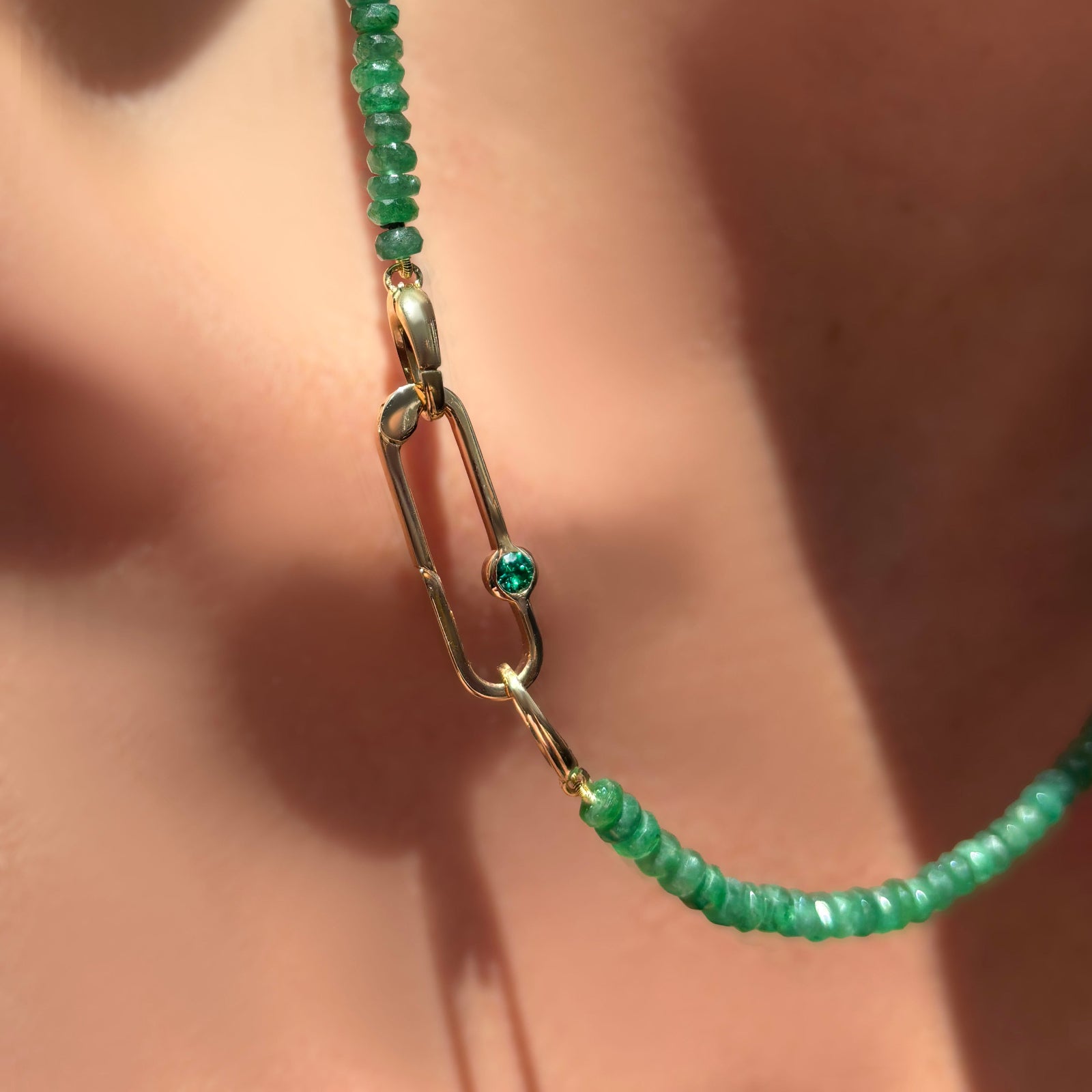 Faceted Emerald Necklace with paperclip charm lock with emerald gemstone on a model's neck.