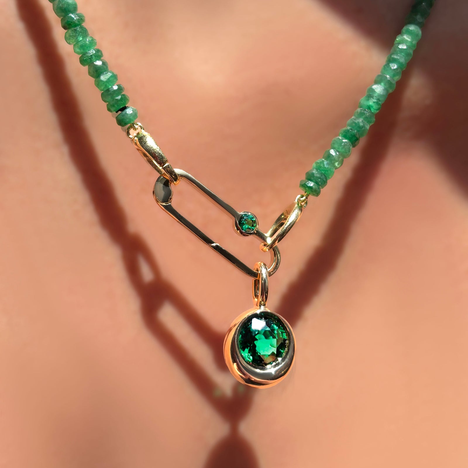 Faceted Emerald necklace with paperclip charm lock with emerald gemstone dangling a molten solitaire charm with round emerald on a model's neck.