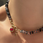 Faceted rutilated quartz necklace with triple link charm lock, molten solitaire charm with ruby, and letter charm on the neck.