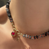 Faceted rutilated quartz necklace with triple link charm lock, molten solitaire charm with ruby, and letter charm on the neck.