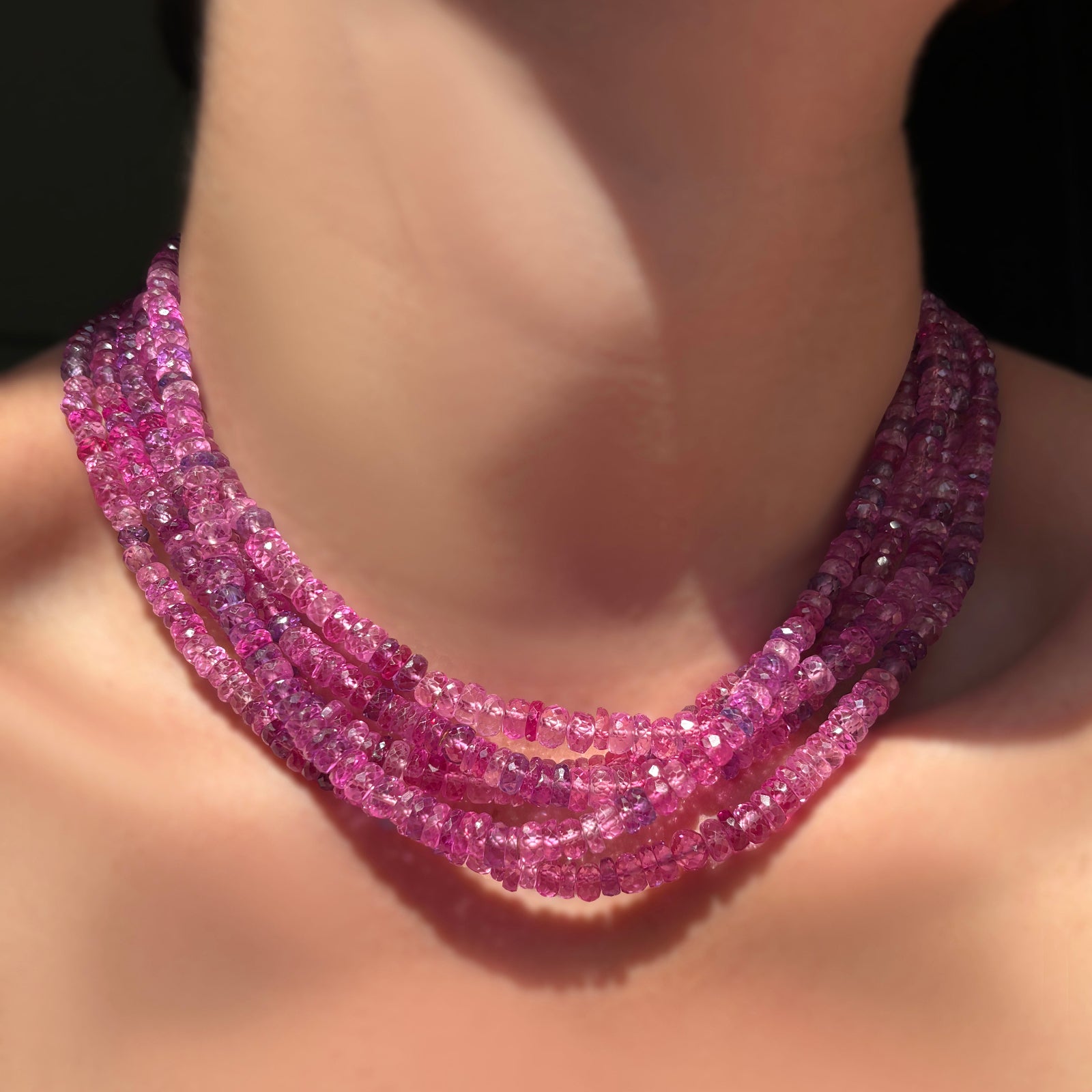 Stack of fuchsia faceted sapphire necklaces on a model's neck.