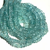 A pile of faceted aquamarine rondelle necklaces in sunlight on a white background.