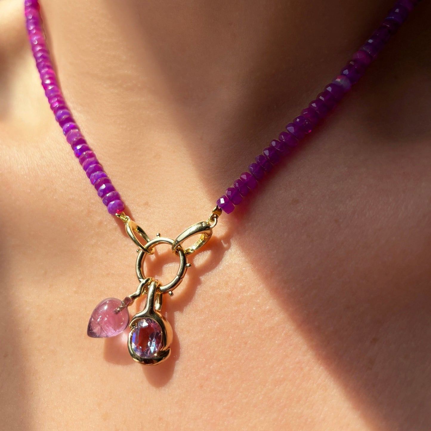 Molten knot charm with gemstone. Styled on a neck hanging from a beaded round charm lock on a beaded necklace.