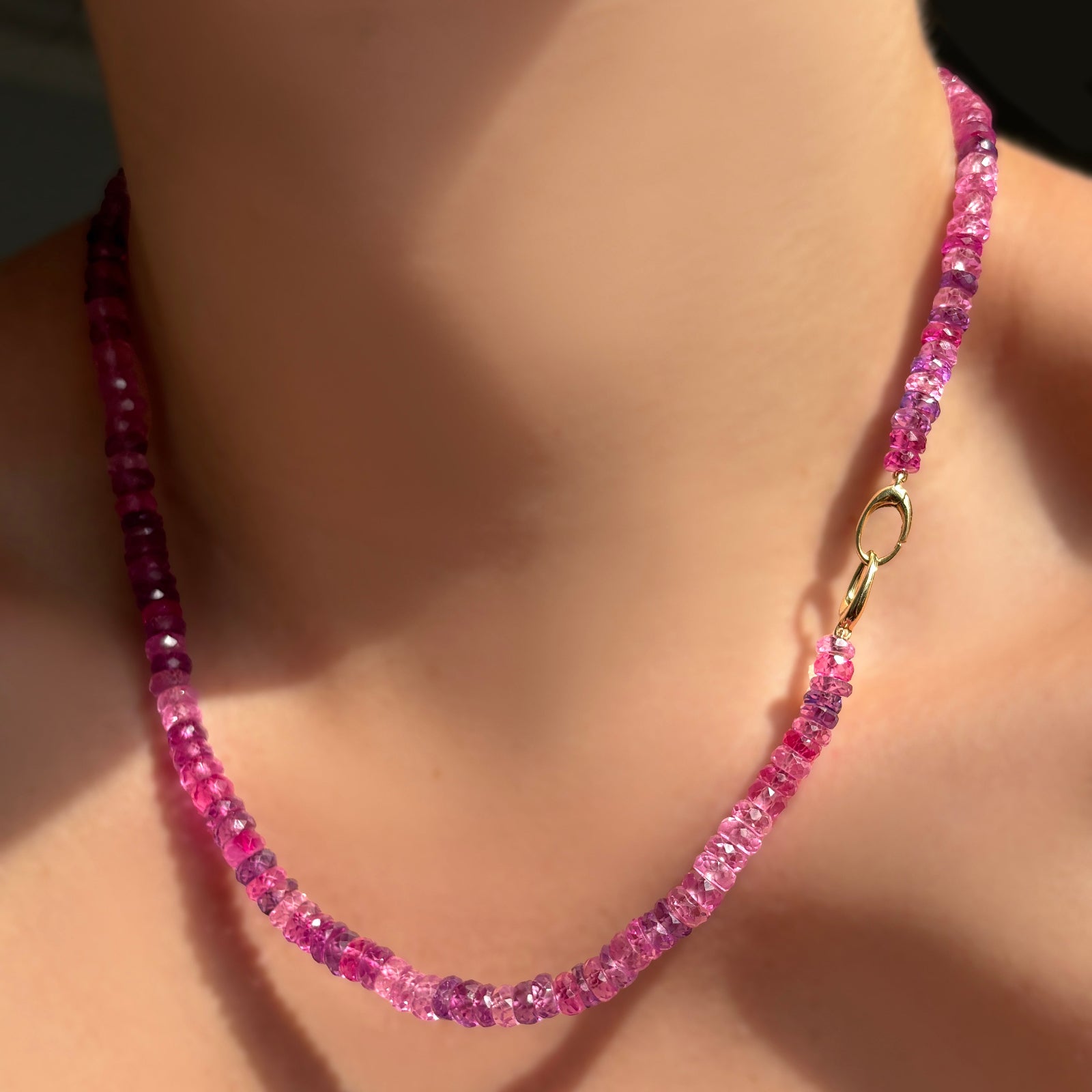 fuchsia faceted sapphire necklace with linking ovals clasp in 14k yellow gold facing front on a model's neck.
