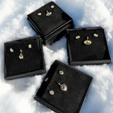 Gift boxes of molten solitaire charms and studs in the snow for the holidays.