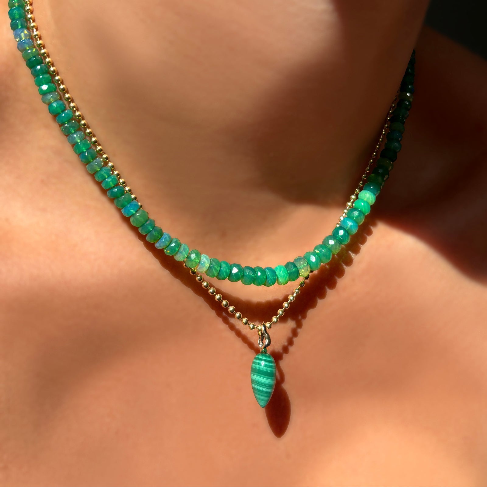 grass green faceted opal necklace with malachite drop charm on yellow gold bead chain on a model's neck.