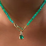 A green faceted opal necklace with yellow gold linking ovals clasp, holding an emerald charm lock with a molten knot charm with rose cut emerald, hanging from the neck.
