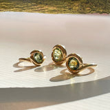 green molten knot rings on white surface with gold branch and shadows