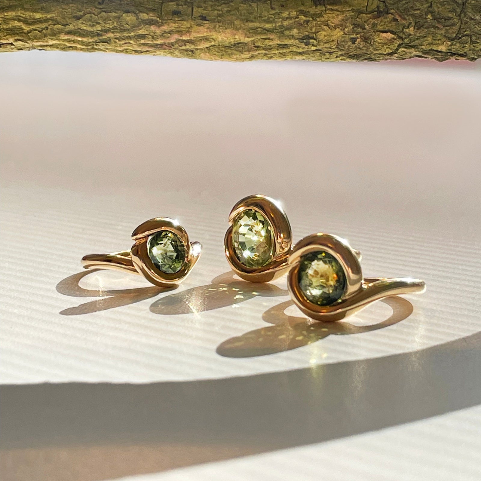 green molten knot rings on white surface with gold branch and shadows