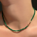 Green faceted emerald necklace with the 14k yellow gold linking ovals clasp towards the front on a model's neck.