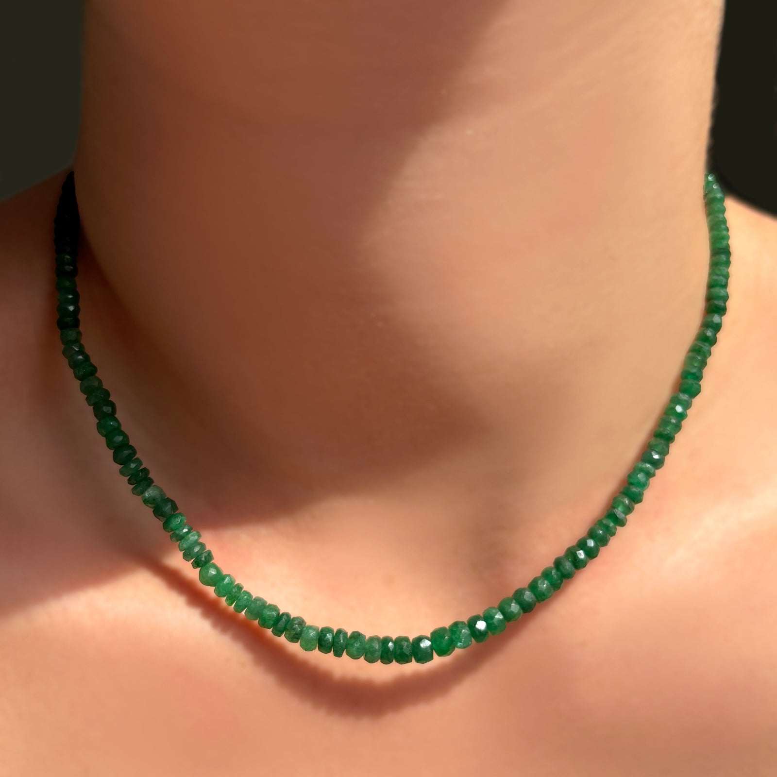 single green faceted emerald necklace on a model's neck.