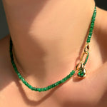 Green faceted emerald necklace with an emerald charm lock and molten knot charm with rose cut emerald on a model's neck.