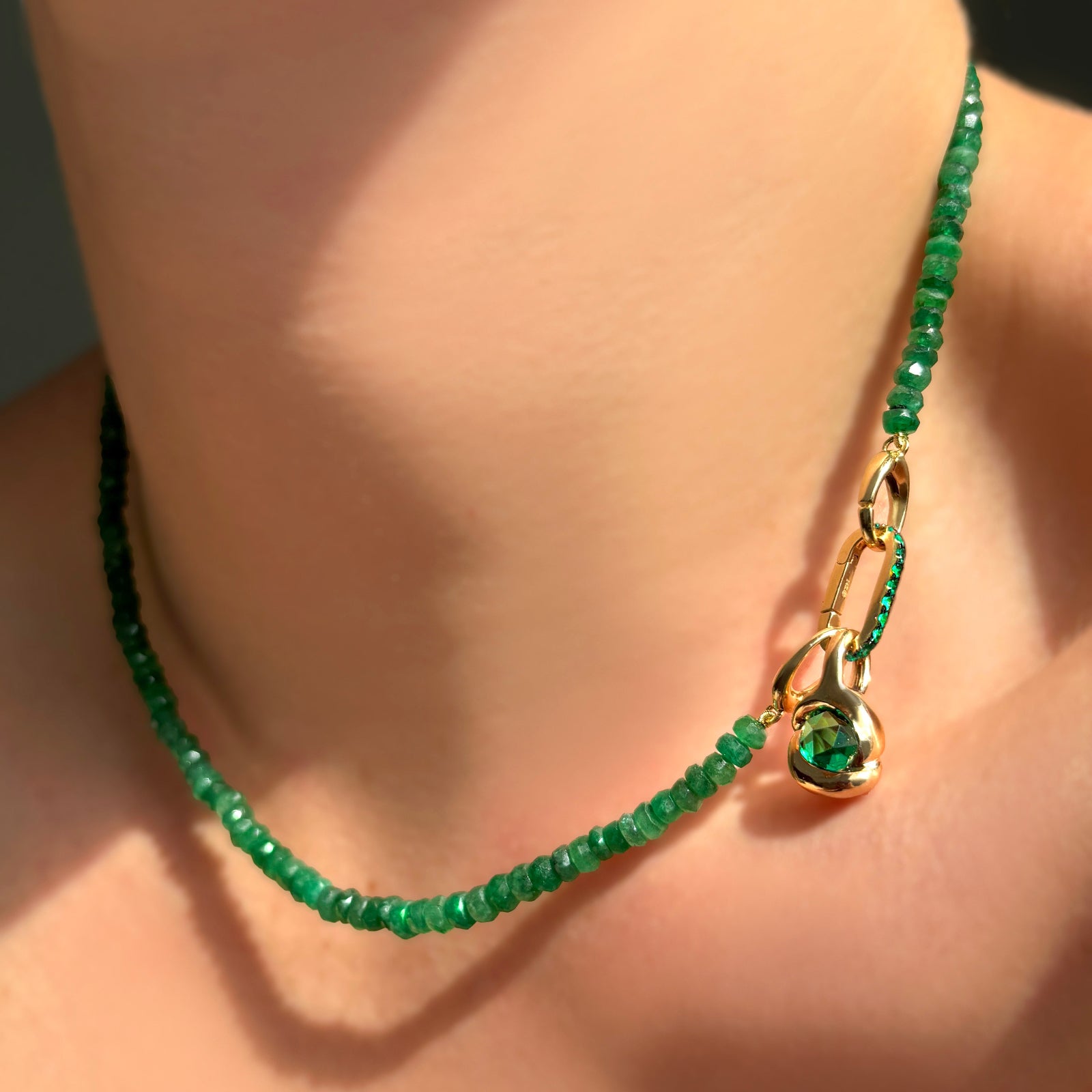 Green faceted emerald necklace with an emerald charm lock and molten knot charm with rose cut emerald on a model's neck.