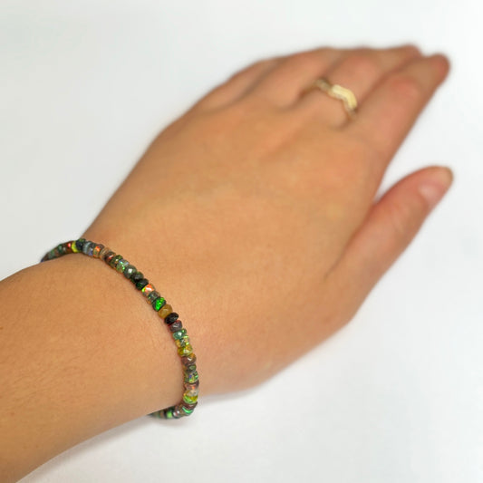 Shimmering beaded bracelet made of faceted opals in shades of green, yellow, black, and clear on a gold linking lobster clasp. 