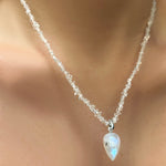 A herkimer necklace hangs on a model's neck. From it is strung a moonstone drop charm with a 14K recycled white gold moonstone drop charm.