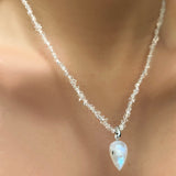 A herkimer necklace hangs on a model's neck. From it is strung a moonstone drop charm with a 14K recycled white gold moonstone drop charm.