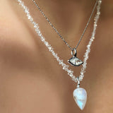 A moonstone drop charm with a 14K ripple bale hangs on a herkimer diamond necklace on a model's neck. It is staggered w th a diamond cut bead chain necklace with a molten marquise diamond solitaire charm, both are 14K white gold.