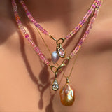 Hibiscus Sapphire Necklace with blue lace agate drop charm and molten knot charm with amethyst layered over another sapphire necklace with molten solitaire charm with pear shaped diamond, over a diamond cut bead chain with blush baroque pearl charm on a model's neck.