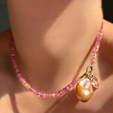 Hibiscus Sapphire Necklace with its Evolution Clasp turned toward the front holding a blush baroque pearl and molten knot charm with amethyst.
