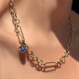 Irregular cable chain necklace in 14k yellow gold with a paperclip charm lock with sapphire and molten knot charm with star sapphire on a model's neck.