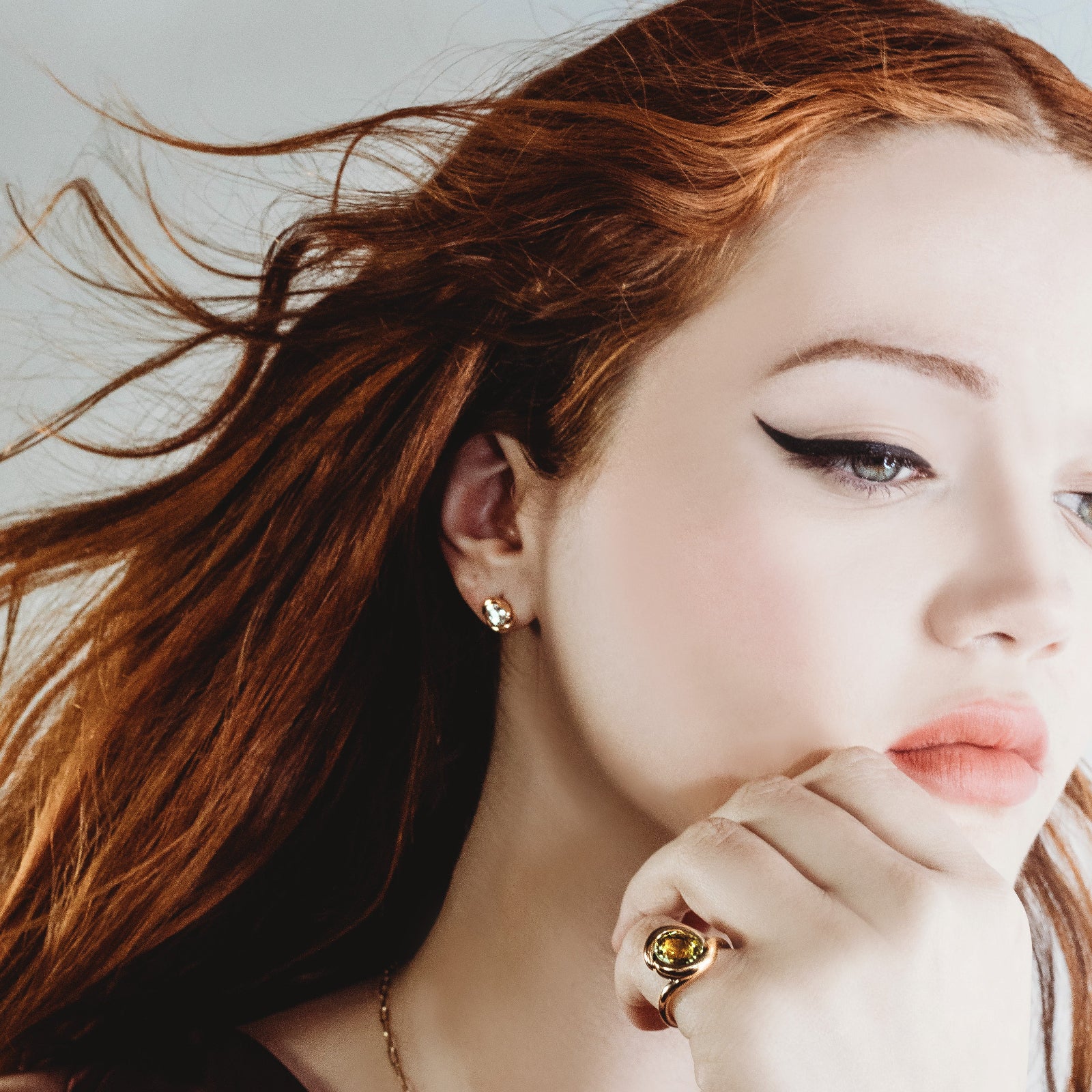Molten knot ring with green tourmaline on a model with red hair, blowing in the wind.
