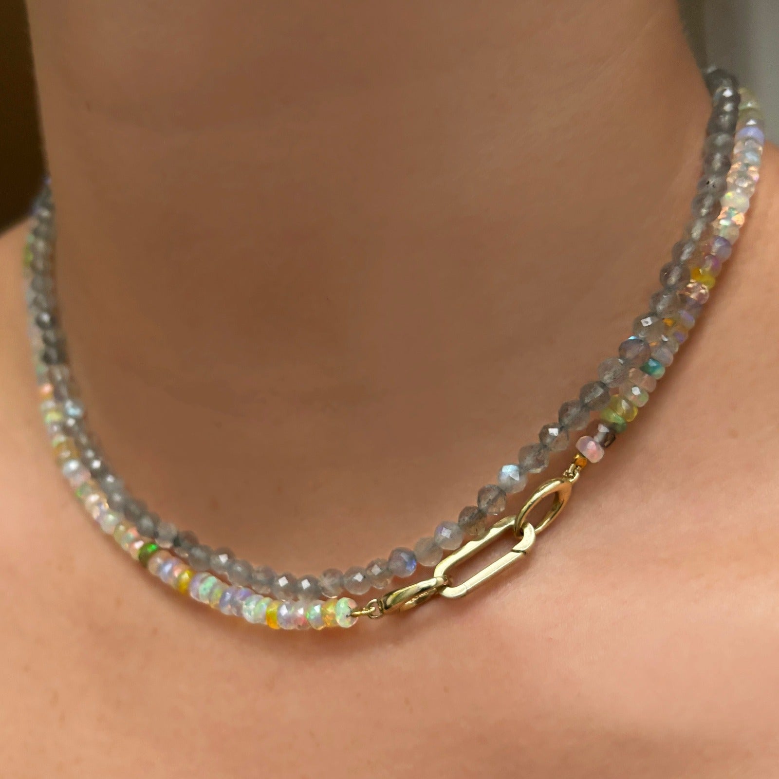 14k yellow gold oval locking charm styled on a neck locked onto oval clasps of a beaded necklace.