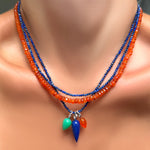 Two slim lapis necklaces with a chrysoprase, lapis, and carnelian drop charm with recycled sterling silver ripple bales layered with a faceted carnelian necklace on a model's neck.