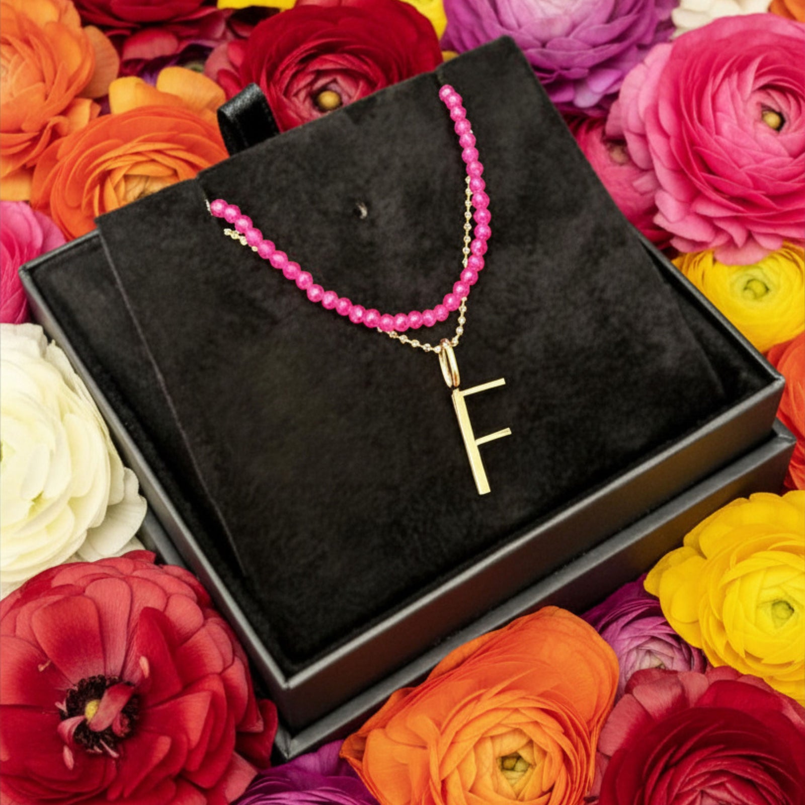 layered necklace bundle with slim ruby necklace and letter F charm on ranunculus