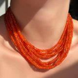 Multiple layered strands of faceted carnelian necklaces on a model's neck.