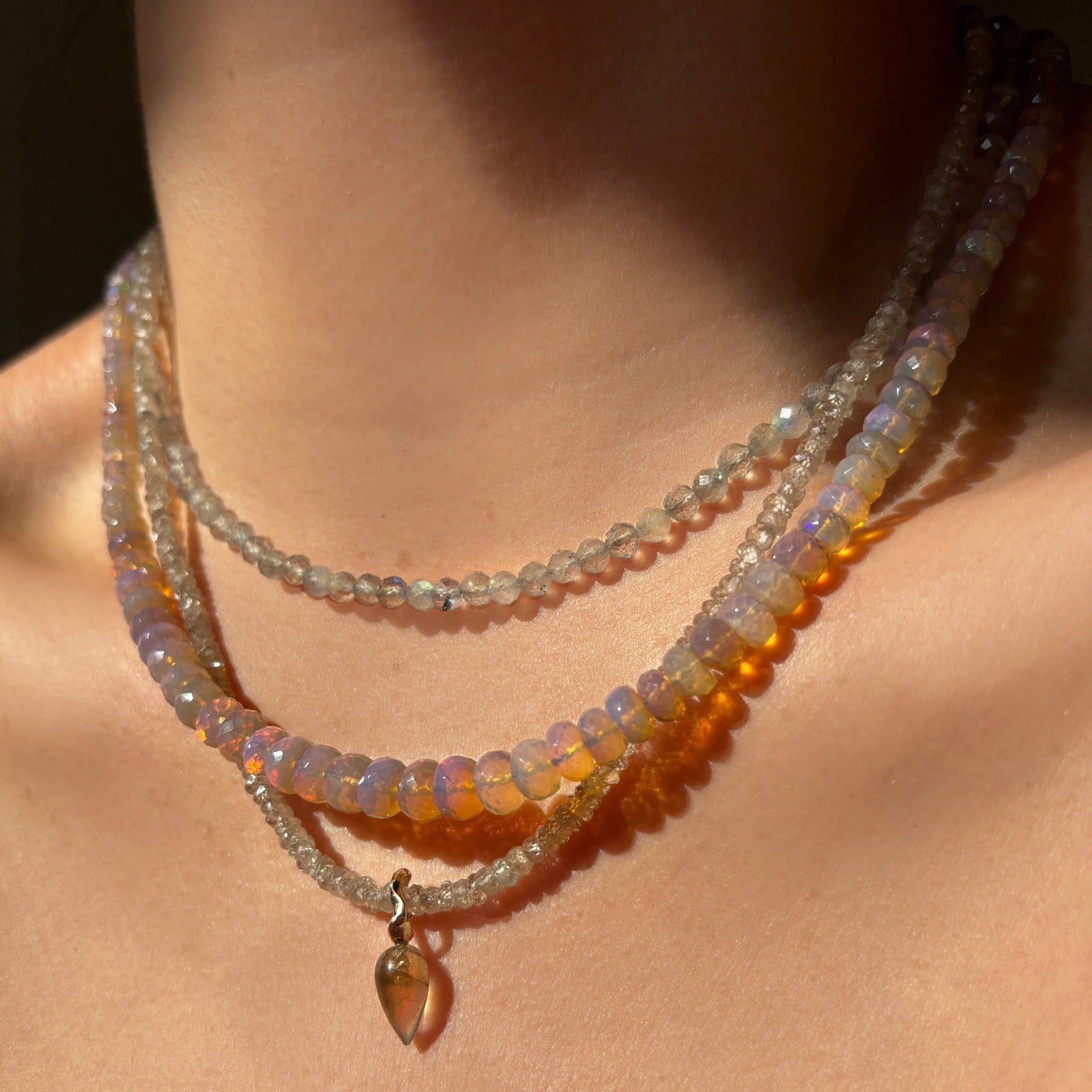Shimmering beaded necklace made of faceted opals in shades of clear and light lilac on a gold linking ovals clasp. Styled on a neck with an acorn drop charm.