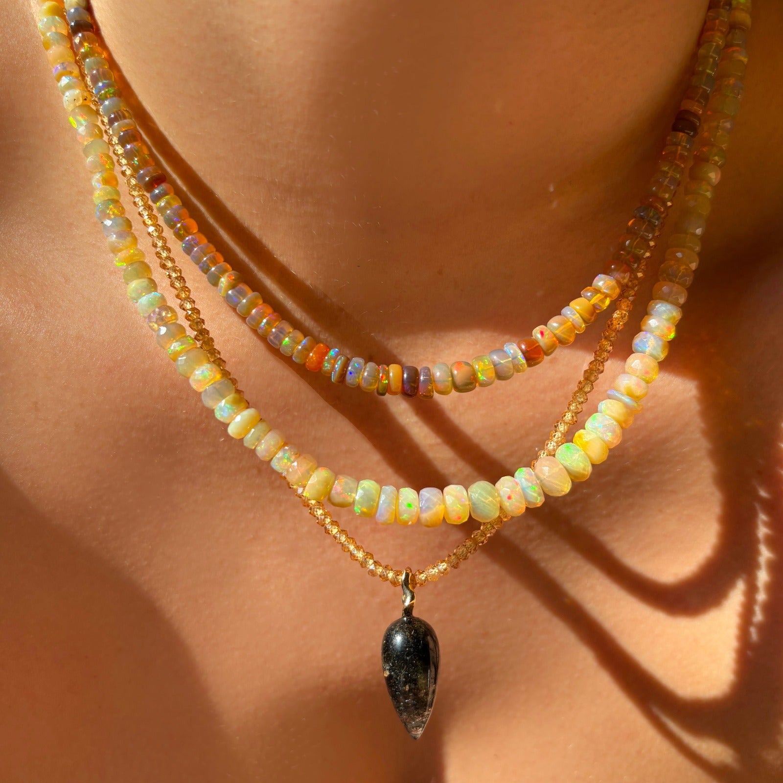 Shimmering beaded necklace made of faceted opals in shades of pastel yellow and clear opals on a gold linking ovals clasp. Styled on a neck layered with an acorn drop charm.